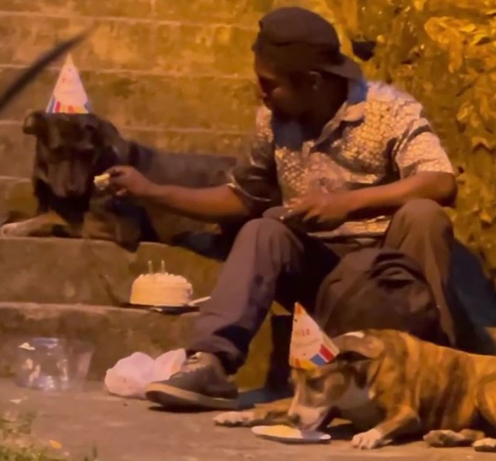 Un sans-abri fête l'anniversaire de son chien avec un gâteau et une chanson assis sur les marches d'un parc